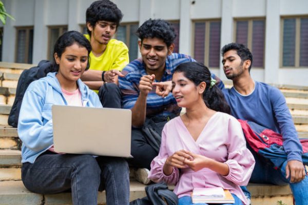 Group of happy students checking results on laptop while sitting on college campus - concept of education, technology and project work discussion